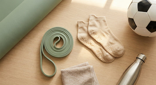 A flat lay overhead shot of anti-slip grip socks surrounded by athletic accessories including a yoga mat, soccer ball, and resistance band on a light wood surface.
