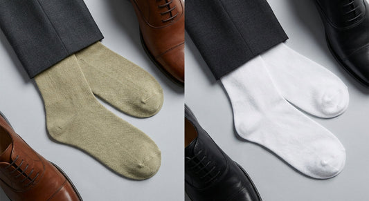 A flat lay editorial photo comparing two pairs of dress socks in contrasting textures, styled alongside polished dress shoes and tailored trouser hems on a slate surface.