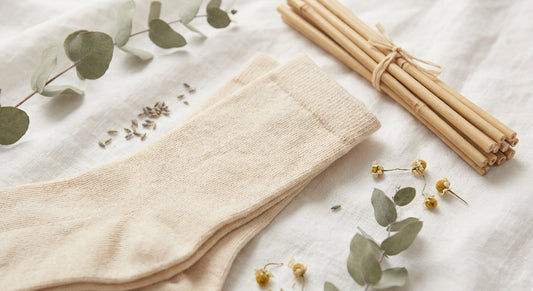 Soft bamboo fiber socks resting on white linen alongside dried botanicals and raw bamboo stalks in warm natural light.