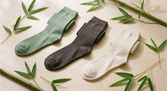 A flat lay of premium bamboo socks in earthy tones arranged on a light wood surface with bamboo stalks as natural accents.