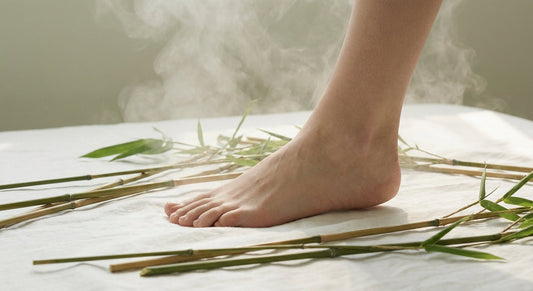 A bare foot resting on a white surface surrounded by fresh bamboo stalks with soft mist dissipating around it, evoking moisture control and foot health.