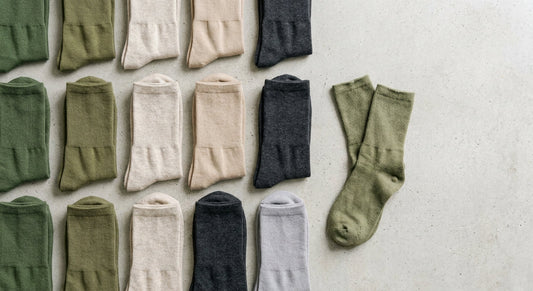 A flat lay of neatly folded fresh bamboo socks arranged on a light concrete surface, with one worn pair set apart to contrast against the newer ones.