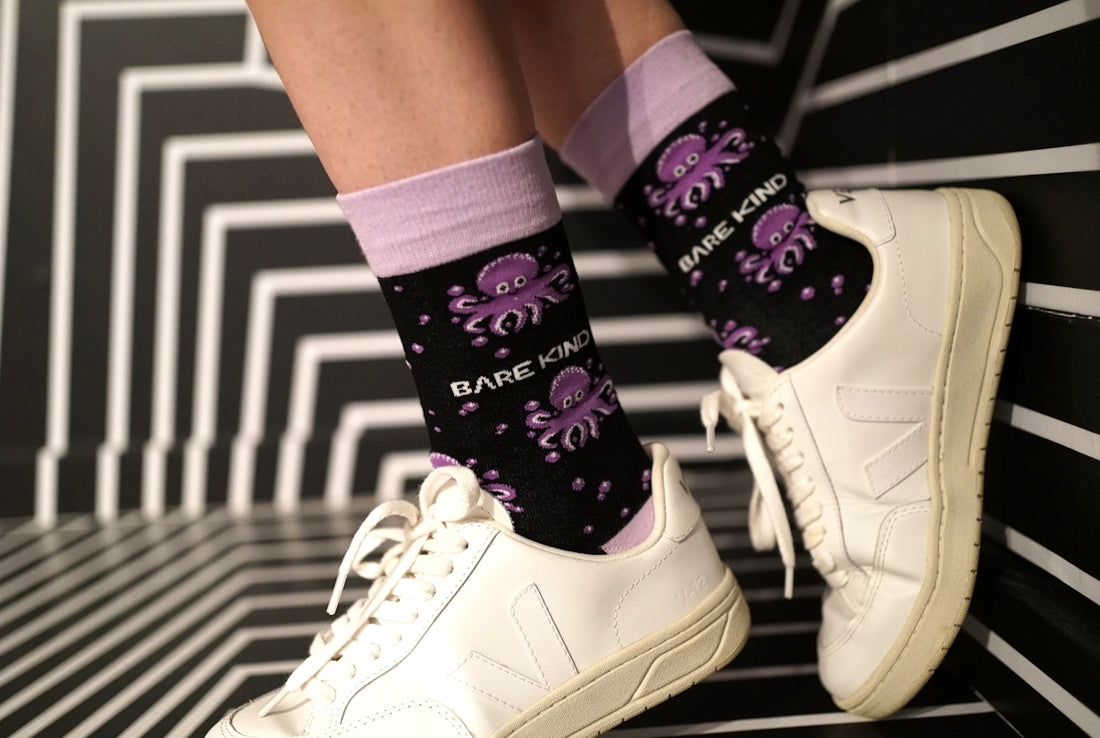A person wearing white sneakers and purple socks
