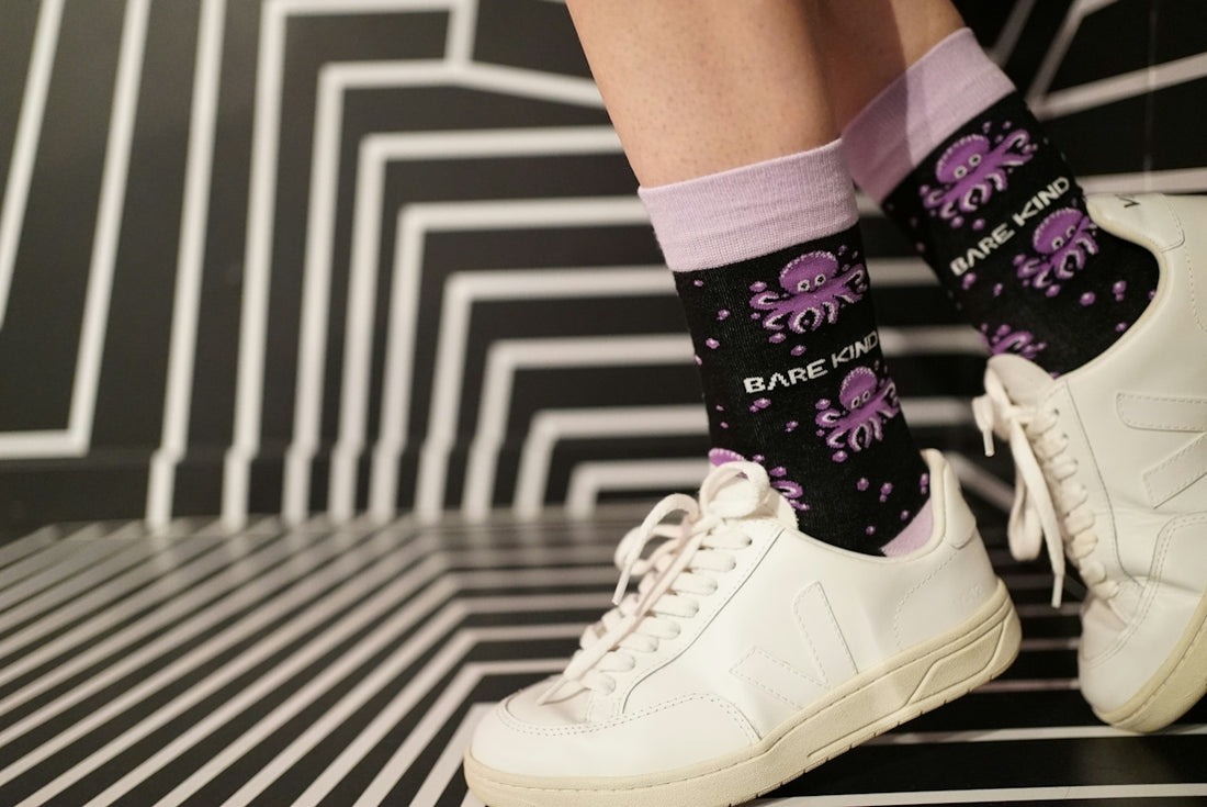A person wearing white sneakers and purple socks