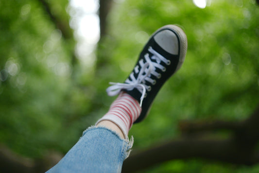 Leg with black sneaker and striped sock against green foliage