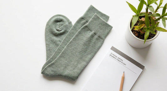 A flat-lay editorial photo of soft green bamboo-fiber socks beside a notepad and small bamboo plant on a white surface, evoking clinical foot health expertise.