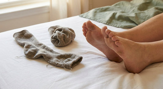 A pair of bare feet resting beside a discarded, worn-out pair of stretched and misshapen socks on a clean white surface.