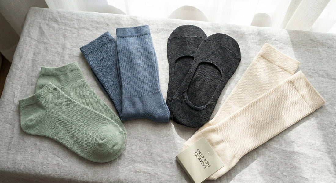 Four different sock styles — ankle, crew, no-show, and compression — arranged in a clean flat lay on a light linen surface, showcasing a range of premium bamboo fiber hosiery.
