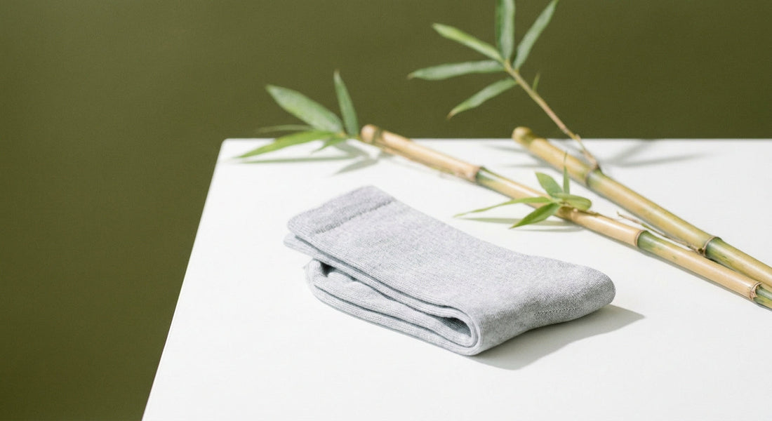 A pair of folded grey crew socks resting beside fresh bamboo stalks and leaves on a clean white surface, evoking natural breathability and freshness.