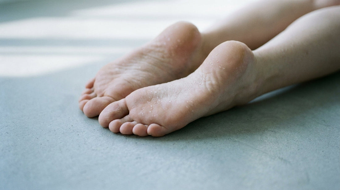 Close-up of bare feet on a cool concrete surface with subtle moisture droplets on the skin, lit by soft natural light.