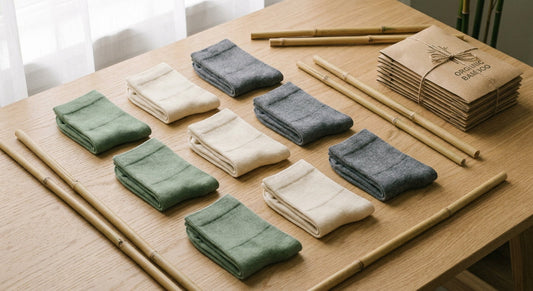 A flat lay of neatly folded bamboo socks in earth tones arranged on a light wood surface alongside bamboo stalks and kraft-paper wrapped bundles.