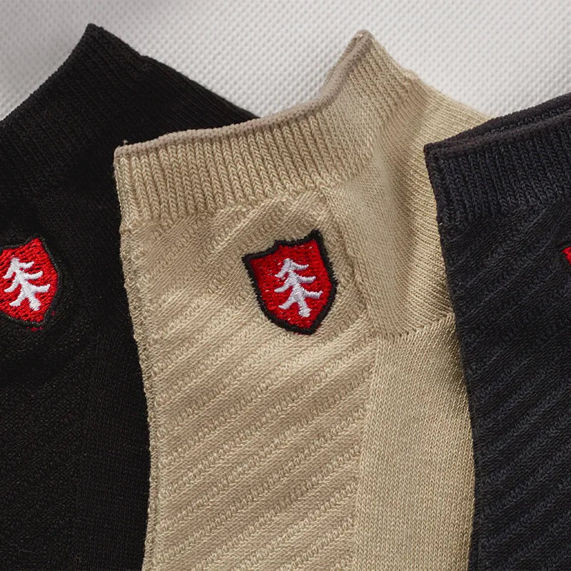 Three pairs of ribbed socks in black, tan, and dark gray with embroidered logo patches.